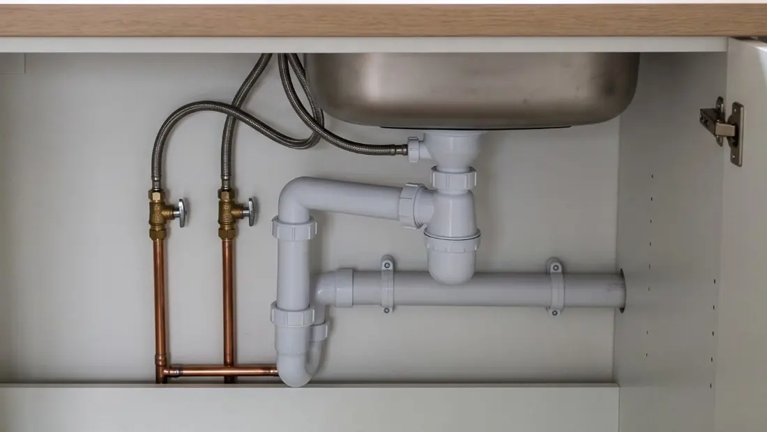 Siphon et évacuation sous un évier, raccords en PVC et arrivées d'eau en cuivre